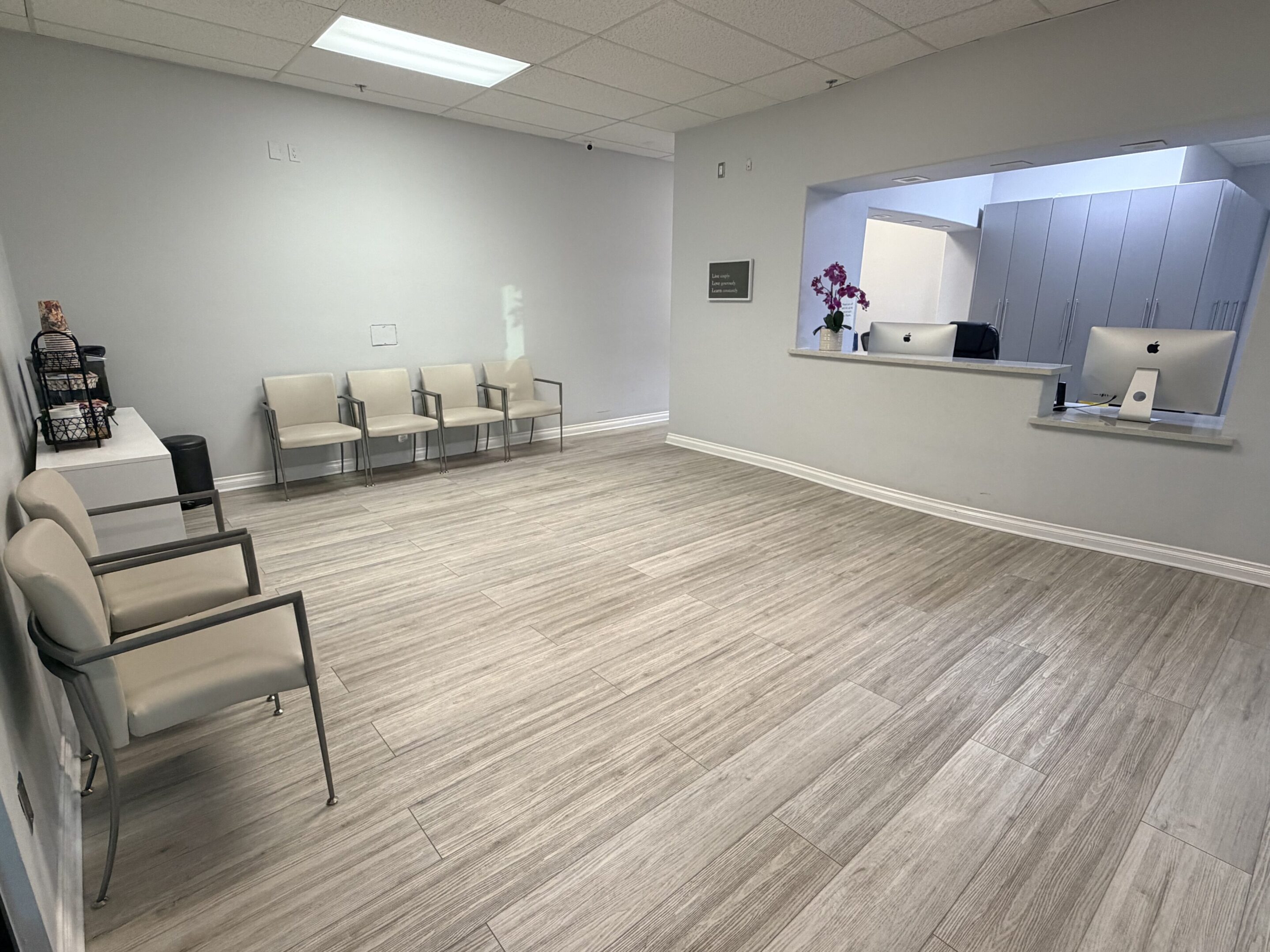 A clean, empty waiting room with chairs and a reception window.